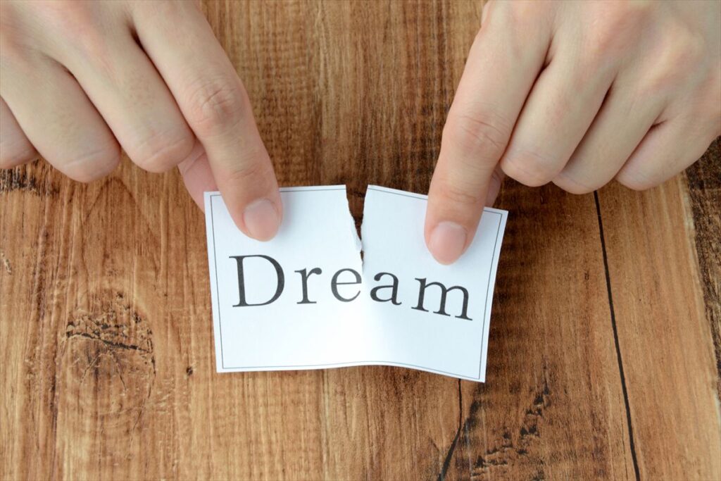 「Dream」と書かれた紙を破っている手元、夢を諦めた瞬間を象徴するイメージ
