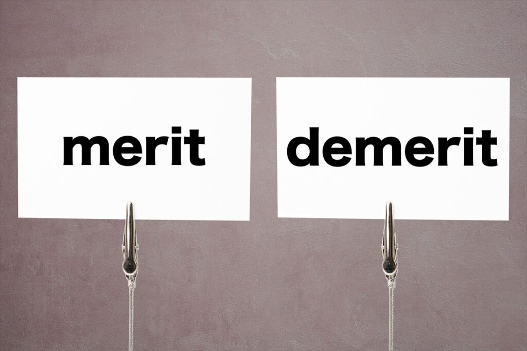 「merit(メリット)」と書かれたカードと、「demerit(デメリット)」と書かれたカードが、それぞれクリップに挟まれて並んで吊るされている。メリットとデメリットの比較を表現している。
